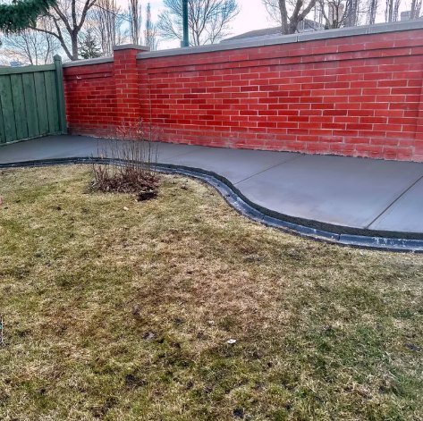 Curved backyard walkway along a brick wall